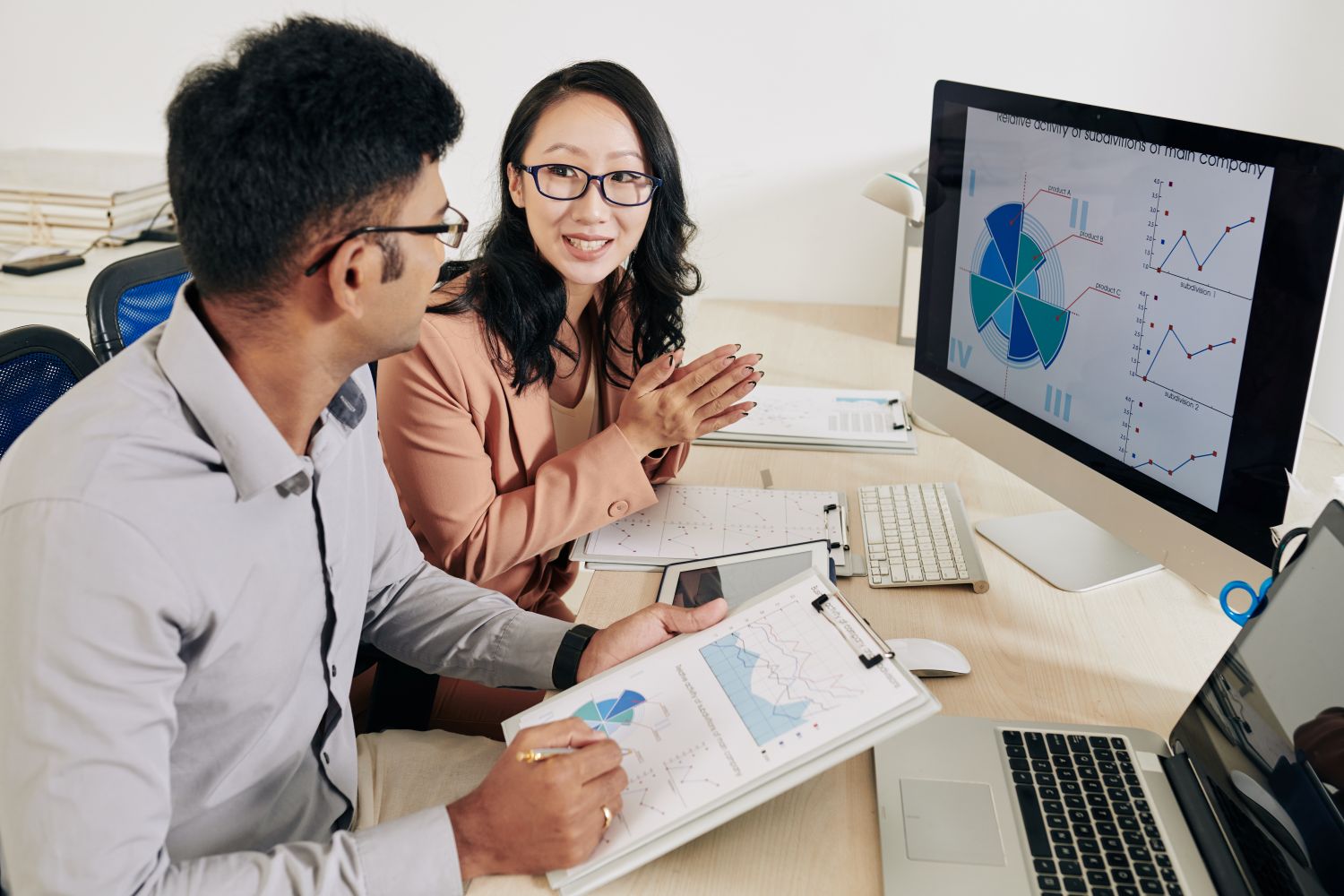 Two Data Analysts reviewing reports on a screen together 